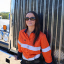 Woman wearing the Syren Brown safety glasses in orange hi-vis work shirt, standing in front of a Kenworth truck